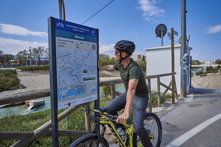 Un ciclista consulta en un poste informativo el itinerario de la Red Eurovelo en la Región